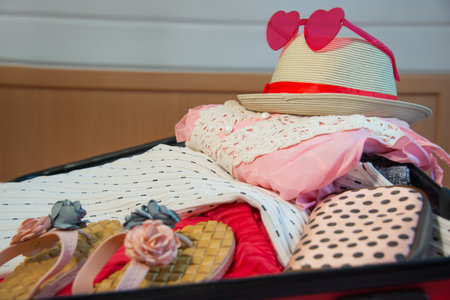 Preparation for summer holidays vacations: open suitcase full of female slippers shoes, beach clothes, cosmetic bag with straw hat and pink sunglasses. Packing things for the journey.の写真素材