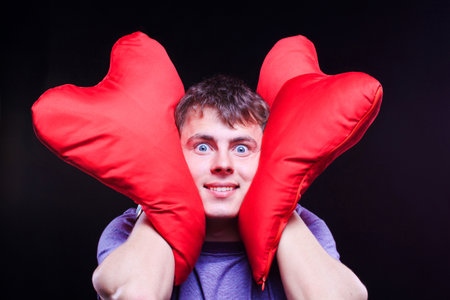 Man holding two red heart-shaped pillows on the black backgroundの写真素材