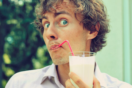 Portrait of funy curl man drinking through pink strawの写真素材