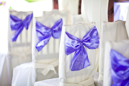 White wedding chairs decorated with purple bowsの写真素材