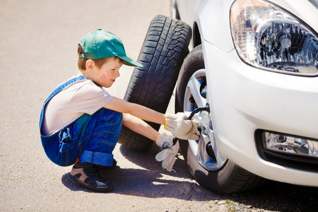 little boy repairing a car on the roadの写真素材