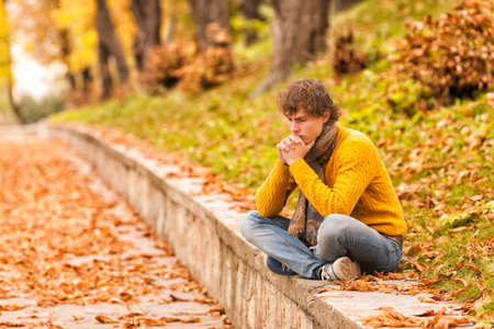 sad curly man siting outdoor on autumn and thinkingの写真素材