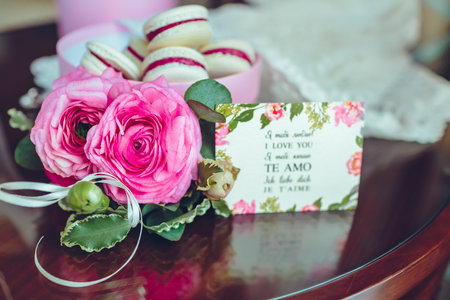 Roses and french macaroon cake. Colorful macaroons in a box with flowers beside on wooden table.の写真素材