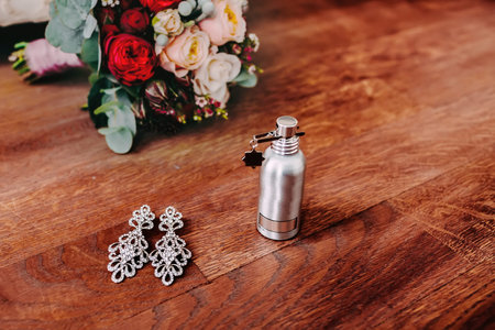 Bridal attributes such as elegant silver earrings with gem and perfume stand next to the wedding...