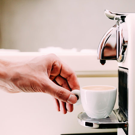 Close up of hand of barista brewing coffee using a coffee machine. The man is standing and holding a white cupの写真素材