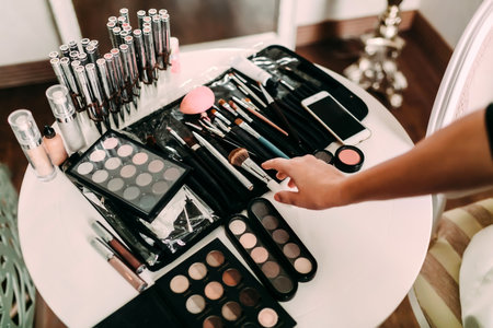 Hands of a makeup artist. Many cosmetics and brushes on a table in the salon. Workplace makeup artist.の写真素材
