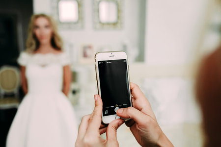 A woman is photographing bride through mobile phone at the wedding. Telephone photo. Focus on the phoneの写真素材