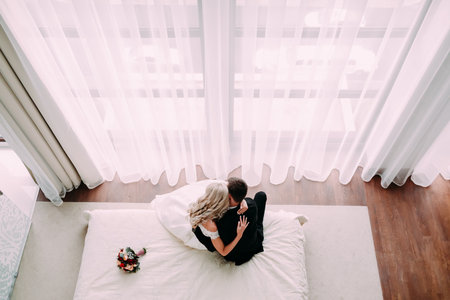 Newlyweds embracing on the bed in the luxury light hotel roomの写真素材