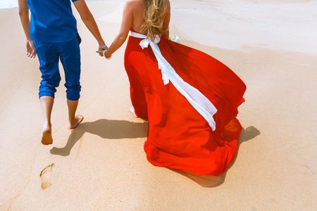 Back view of loving couple walking away with footprints at sandy beach. Holding handsの写真素材