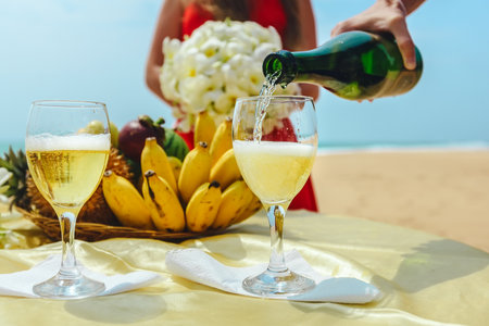 Man is pouring champagne into a glass on a background of a plate with fruit. Celebration on the beachの写真素材