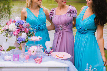 Bridesmaids are hugging and laughing near the festive table at the ceremony. Wedding decoration in the style of boho, floral arrangement in the garden. Close-upの写真素材