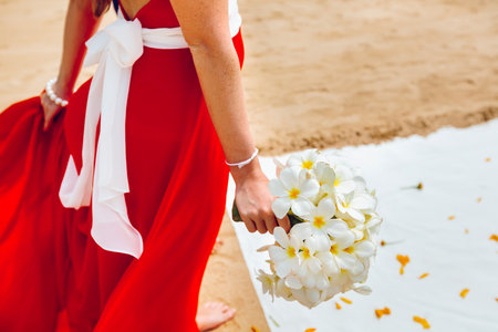 Girl in red fluttering dress holding a white bouquet on the beach, before the wedding ceremony. Close-up, side viewの写真素材