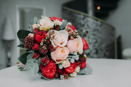 Beautiful bridal bouquet with white and peach roses, red peonies, and other flowers on a white table. Close-up, indoor.の写真素材