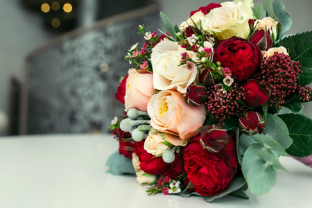 Beautiful bridal bouquet with white and peach roses, red peonies, and other flowers on a white table. Close-up, indoor.の写真素材