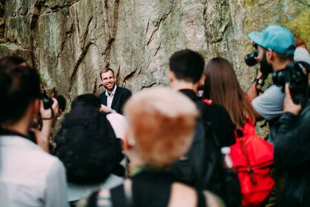 Group of paparazzi people taking picture of a handsome man in nature. Selective soft focus on the guy. Outdoorの写真素材