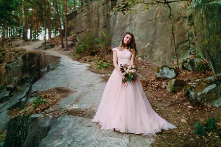 Bride with rustic wedding bouquet stands on the rock. Outdoorの写真素材
