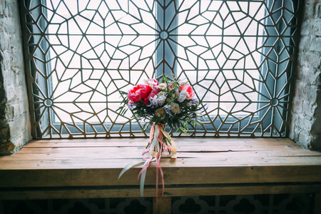 Rustic wedding bouquet with white roses and crimson peonies on a luxury ornament window. Indoors.の写真素材