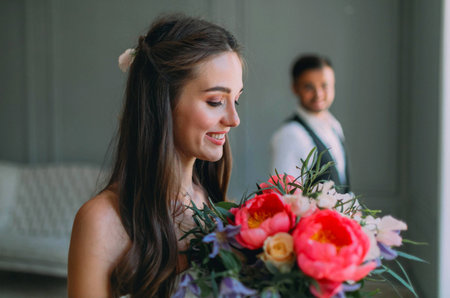 Close-up portrait of cheerful, young bride with a wedding bouquet on blurred groom background. A happy girl with a bunch of flowersの写真素材