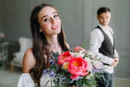 Close-up portrait of cheerful, young bride with a wedding bouquet on blurred groom background. A happy girl posing with a bunch of flowersの写真素材