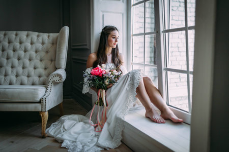 Woman by the window. Bride looking out the window, she waits for the groom. Indoorsの写真素材