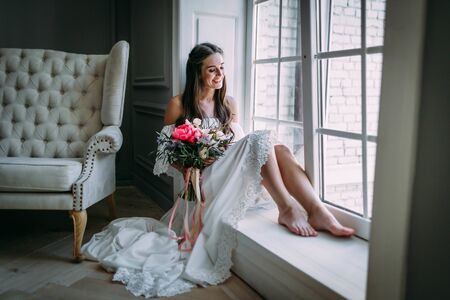 Woman by the window. Bride looking out the window, she waits for the groom. Indoorsの写真素材