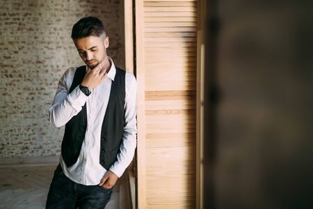 Thoughtful handsome guy in a white shirt and waistcoat near a window. Copy spaceの写真素材