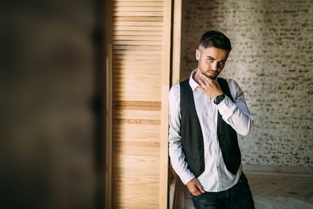 Thoughtful handsome guy in a white shirt and waistcoat near a window. Copy spaceの写真素材