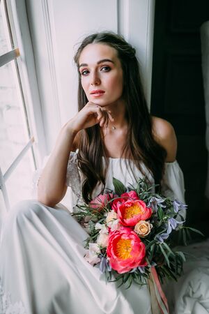 Woman by the window. Beautiful young is bride posing on camera. Close-upの写真素材