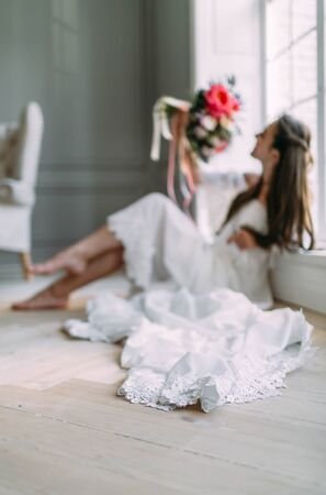 Blurred image of cheerful, young bride which holds a rustic wedding bouquet on panoramic window background. A happy girl with a bunch of flowers, selective focus on the lace of dressの写真素材