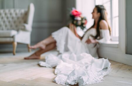 Blurred image of cheerful, young bride which holds a rustic wedding bouquet on panoramic window background. A happy girl with a bunch of flowers, selective focus on the lace of dressの写真素材