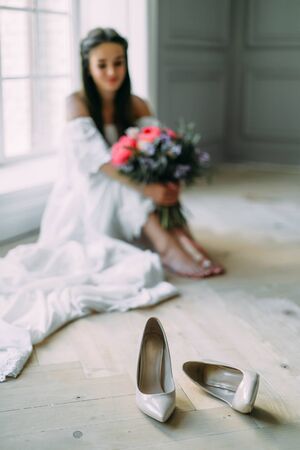 Wedding shoes on a blurred background of cheerful, young bride which holds a rustic bridal bouquet. A happy girl with a bunch of flowers, selective focus on shoesの写真素材
