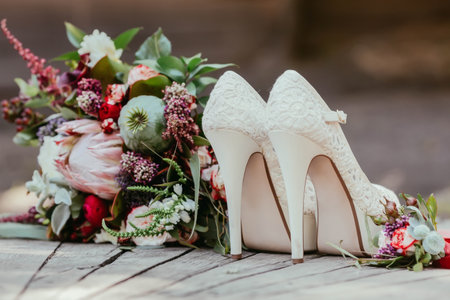 white bridal shoes and rustic wedding bouquet with white and bordeaux roses, peonies, poppy and greens on an aged wooden floor. Artwork, selective focusの写真素材