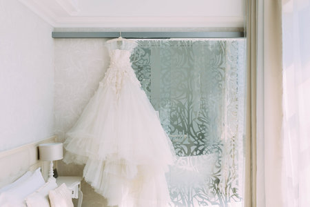 A cream, luxury bridal dress which hangs on the cornice on a background the beige ornate wall. Side viewの写真素材