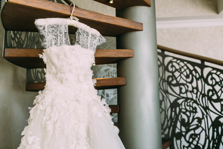 White beautiful bridal dress with lace on a silk shoulders, hanging on a wooden staircase before wedding ceremony. Close-upの写真素材