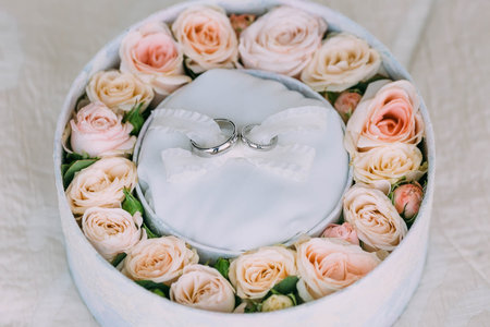 Wedding rings on white background in a pink round box with peach roses. Artwork. Soft focus. Top...