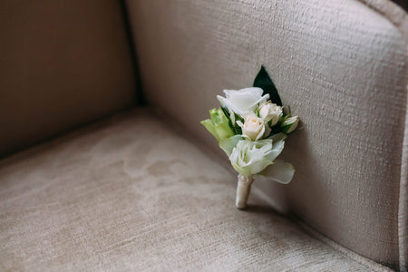 White boutonniere from roses lie on beige armchair. Close-up.