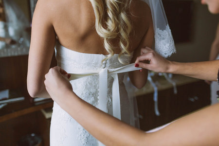 Bridesmaid helps to tie a bow on a wedding dress the bride before the ceremony. Wedding concept. Close-up imageの写真素材