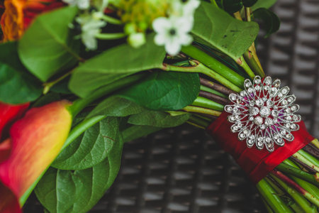 A silver brooch with rhinestones on the stalk of the wedding bouquet with red ribbons. Close-up....