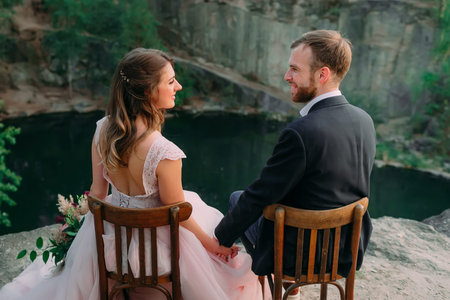 Newlyweds sitting at the edge of the canyon and couple looking each other with tenderness and love. Outdoors weddingの写真素材
