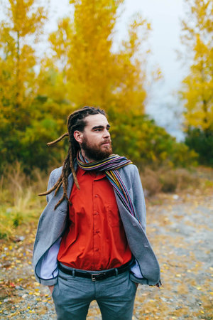 Hipster. A stylish man with dreadlocks and beard in a red shirt and grey jacket. Groom posing on...