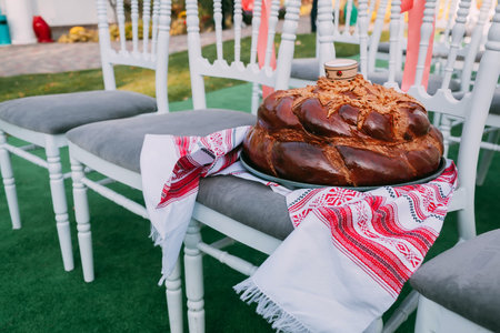 Traditional Ukrainian wedding bread (loaf) in wedding ceremony area. Wooden chairs for guestsの写真素材