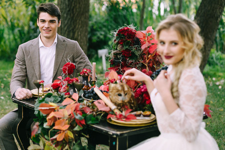 The handsome groom sit at the festive table on blurred bride background. Autumn weddingの写真素材