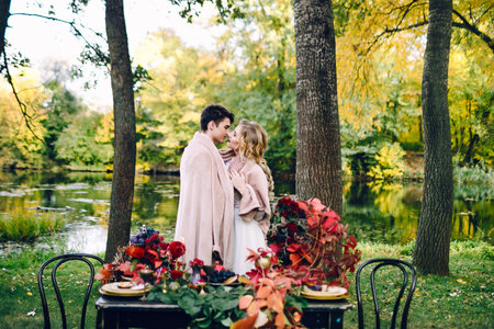 Newlyweds kissing under the plaid next to the festive table. Bride and groom in the park. Autumn wedding. Artworkの写真素材