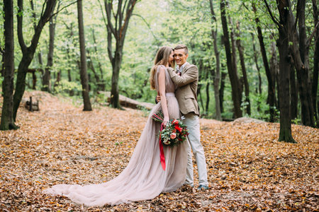 A happy couple is walking on a trail in an autumn forest. Bride and groom are looking at each other on nature.の写真素材