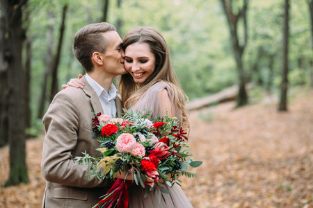 Groom tenderly kissing her beautiful bride in cheek. Autumn wedding ceremony in rustic style. Newlywedsの写真素材