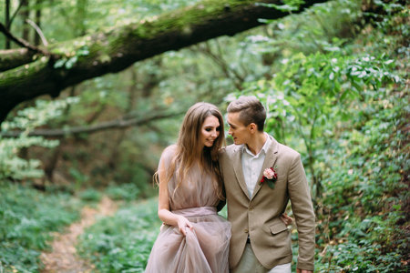 A stylish bride and groom is walking on a trail in an autumn forest. Wedding ceremony outdoors.の写真素材