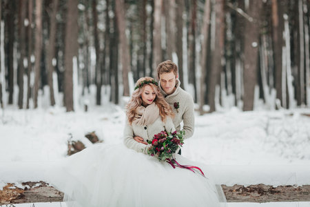 Bride and groom are sitting on the log in the winter forest. Close-up. Winter wedding ceremony.の写真素材