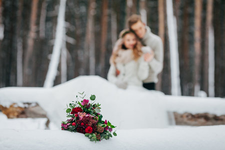 Bride and groom are sitting on the log in the winter forest. Close-up. Winter wedding. Soft focus on the bouquetの写真素材