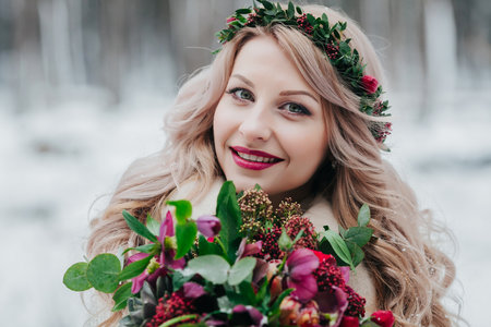 Face of a smiling girl of Slavic appearance with a wreath. Beautiful bride holds a bouquet in winter background.の写真素材