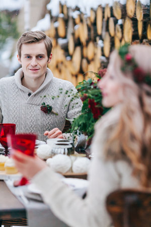 Handsome groom is tenderly looks at his beautiful bride throgh the table. Selective focus on the man. Winter weddingの写真素材